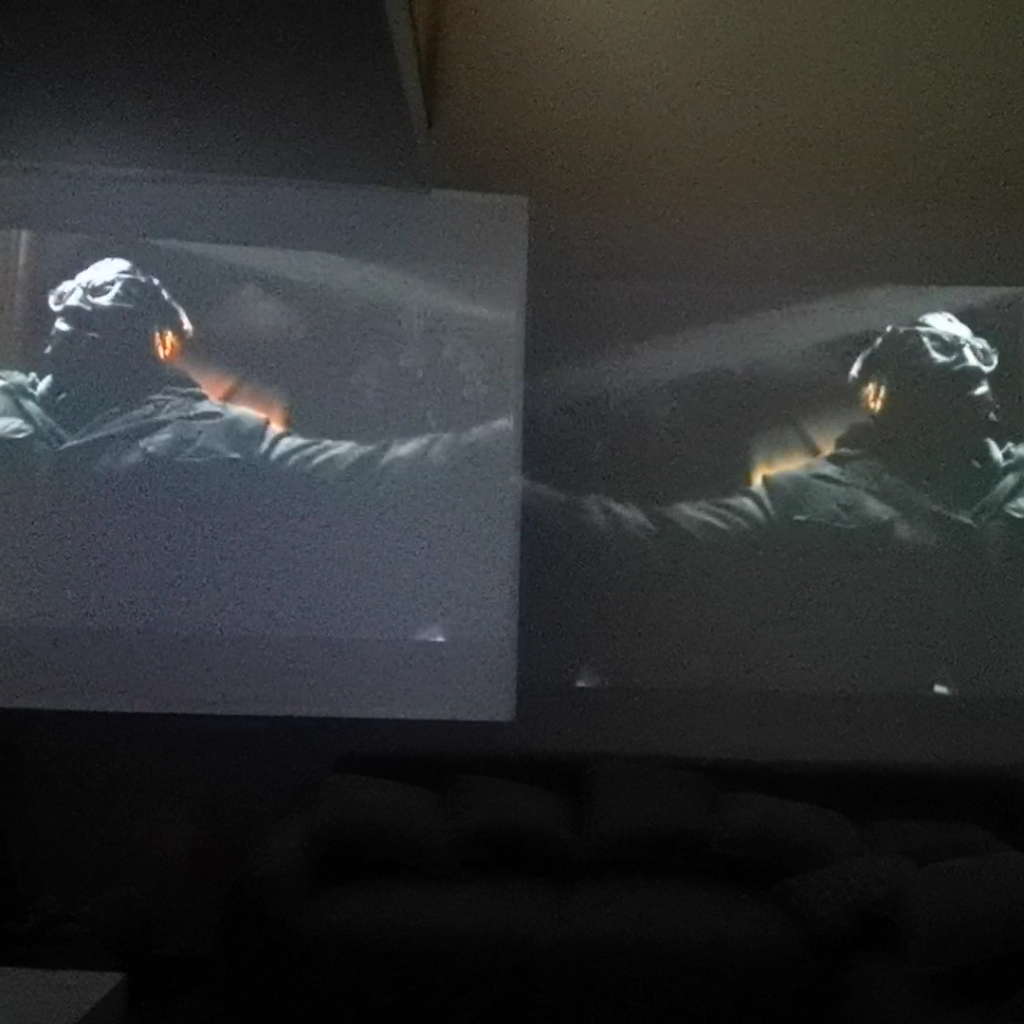 Side-by-side comparison of the Wanbo and XGIMI projectors at 148 inches displaying a dark scene, highlighting the superior black levels of the Wanbo projector on the right.