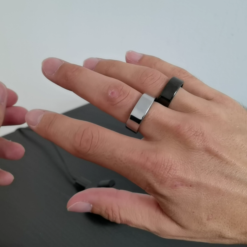 Close-up of Oura Ring showing the signet-ring style design, worn on the middle finger and Xiaomi Smart Ring worn on the ring finger, showcasing its classic rounded appearance